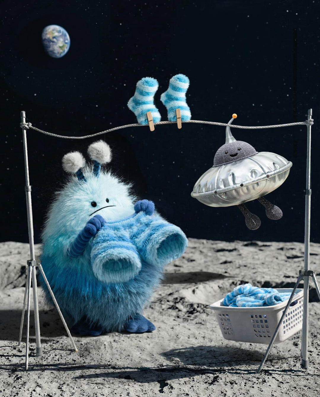 Blue creature on the moon with a laundry basket, space ship, and clothes on a line.