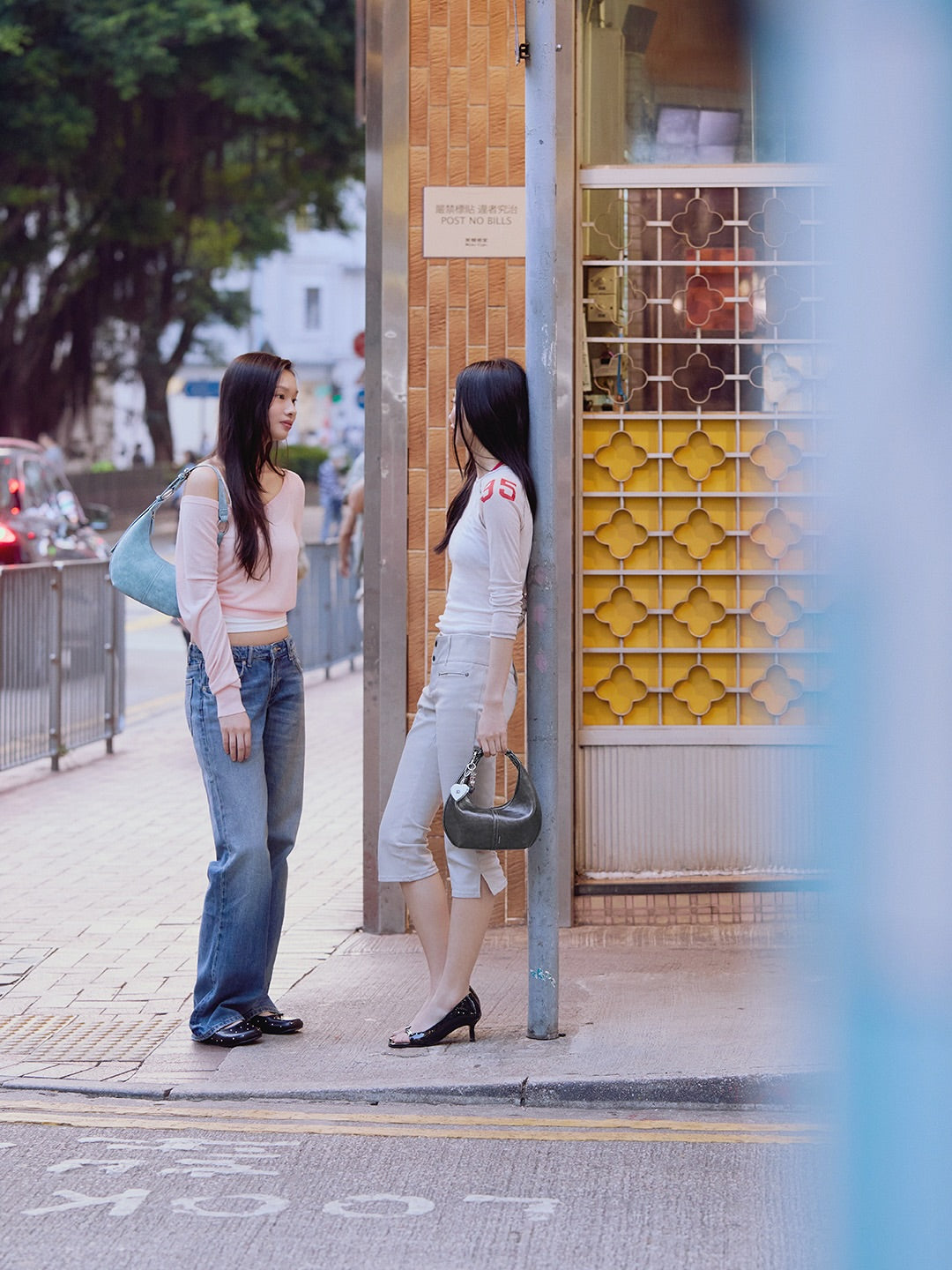 Two women standing on a sidewalk, one looking into a glass booth with a colorful interior.