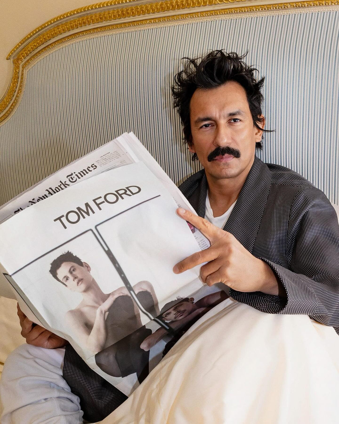Man holding a magazine with Tom Ford cover on a bed