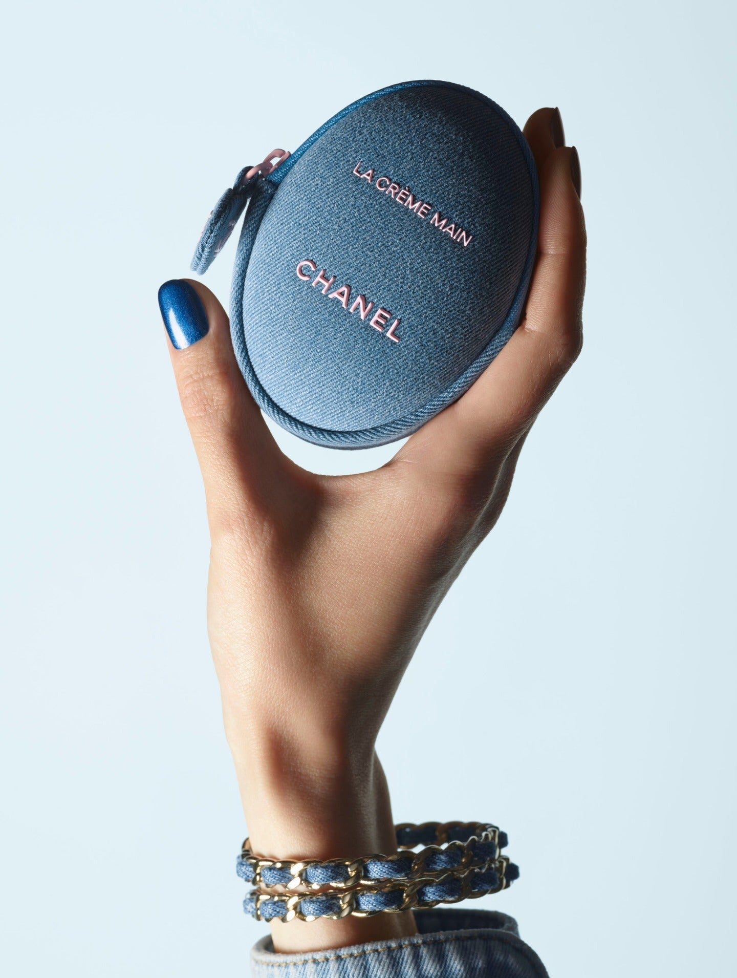 Hand holding a blue Chanel cosmetic case against a light gray background