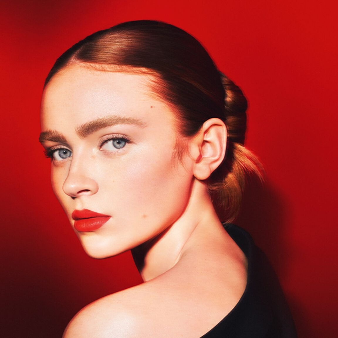 Woman with red lipstick and a black top against a red background